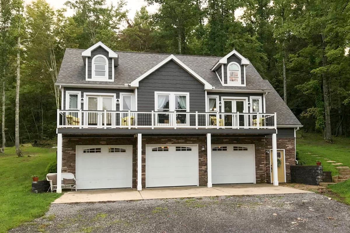 Two-story house plan exterior with a stone veneer and three-car garage. Features include dormers, a balcony, and a gabled roof.