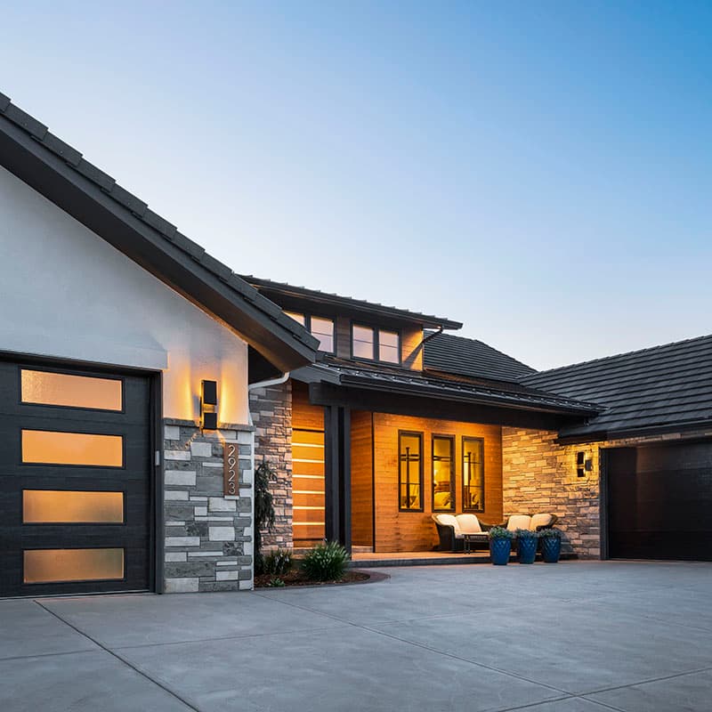 House plan exterior with modern design, stone and wood siding, multiple garage doors, and covered entryway with seating.