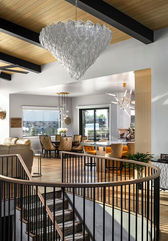 Interior view of open-concept living space with spiral staircase, dining area, and kitchen island. Features wood beams and large chandeliers.