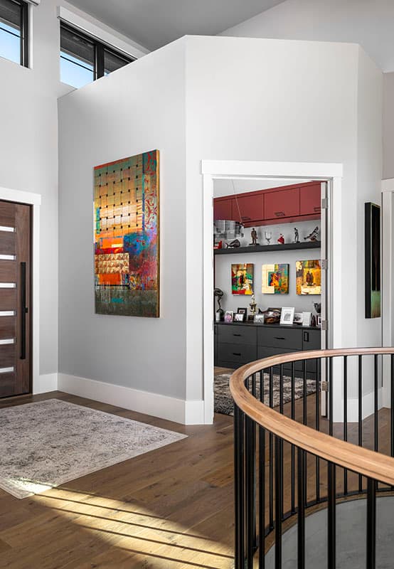 Interior view of a hallway with a modern door, abstract art, and a view into a room with built-in cabinets.