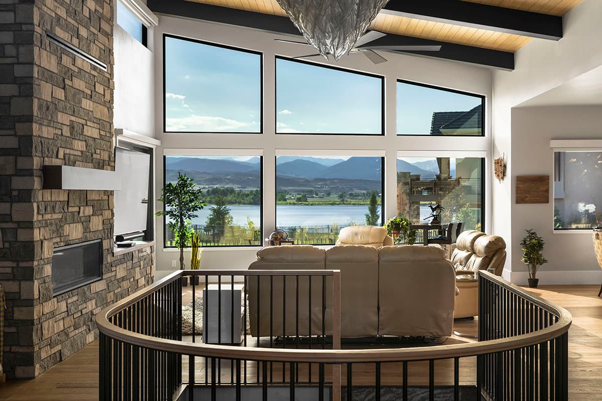 Interior view of living room with stone fireplace, vaulted ceiling, and large windows showcasing mountain and lake views.