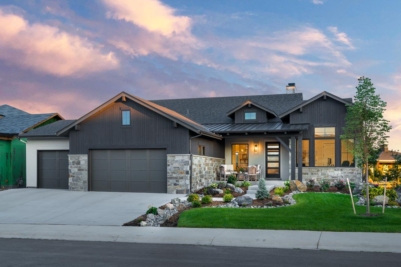 House plan exterior with board and batten siding, stone accents, two-car garage, and a shed-roof porch.