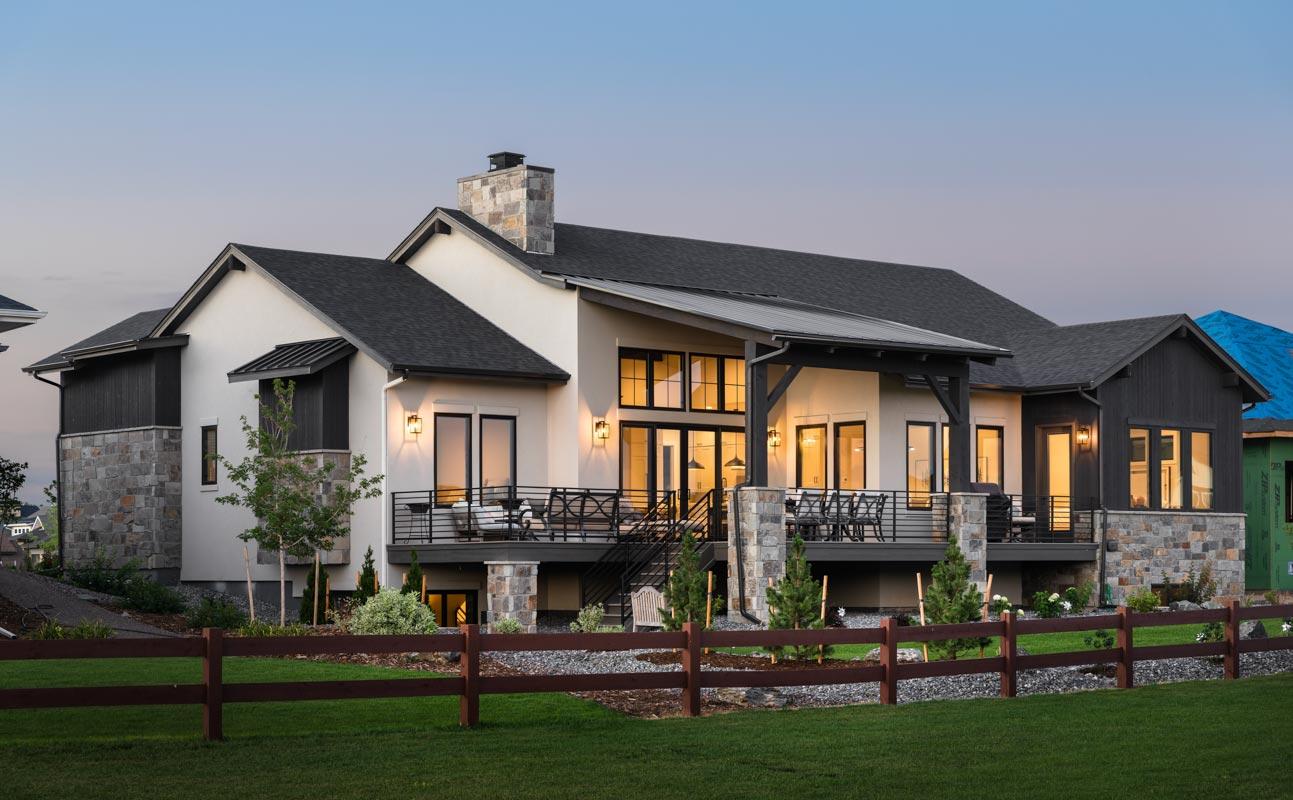 House plan exterior: Modern home with stone and stucco facade, multiple gables, large deck, and expansive windows.