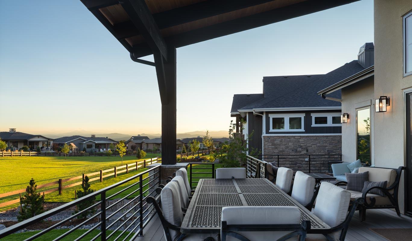 Covered deck with outdoor dining set overlooks landscaped yard and distant mountains. Modern exterior features stone and siding.