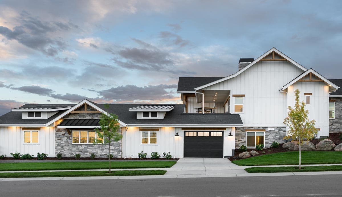 Modern Farmhouse house plan exterior with white board and batten siding, stone accents, gables, dormers, and a dark garage door.