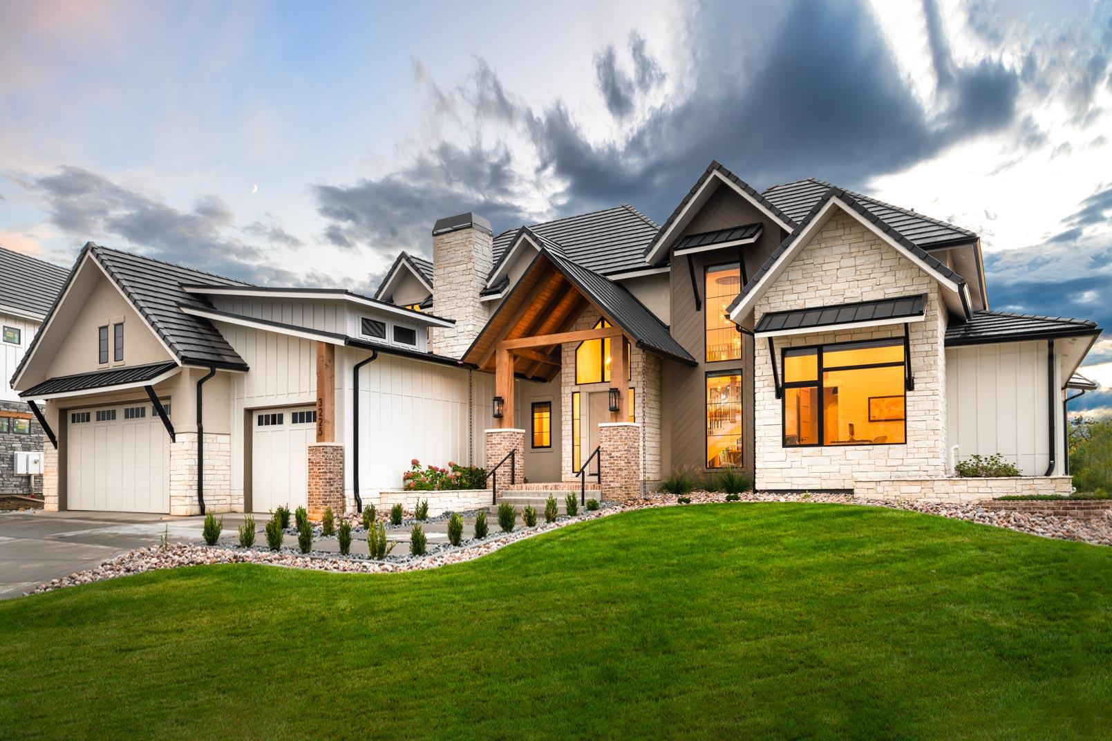 House plan exterior. Modern Farmhouse style, two-story home with multiple gables, stone facade, and a covered porch with a timber frame.