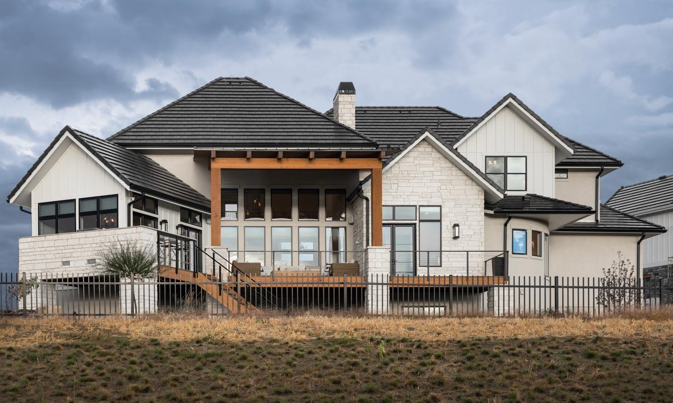 House plan exterior with white stone and board-and-batten siding, multiple gables, covered deck with wood beams, and large windows.