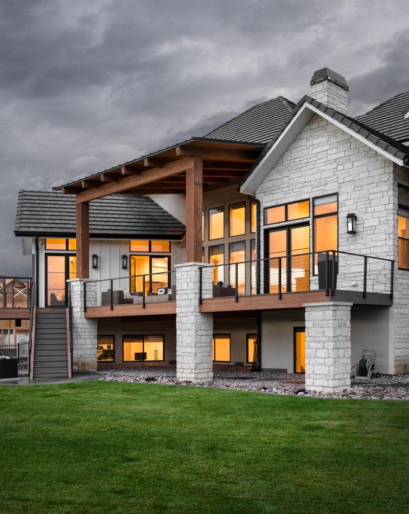 Modern house plan exterior with stone facade, large windows, covered patio, and multi-level decks.