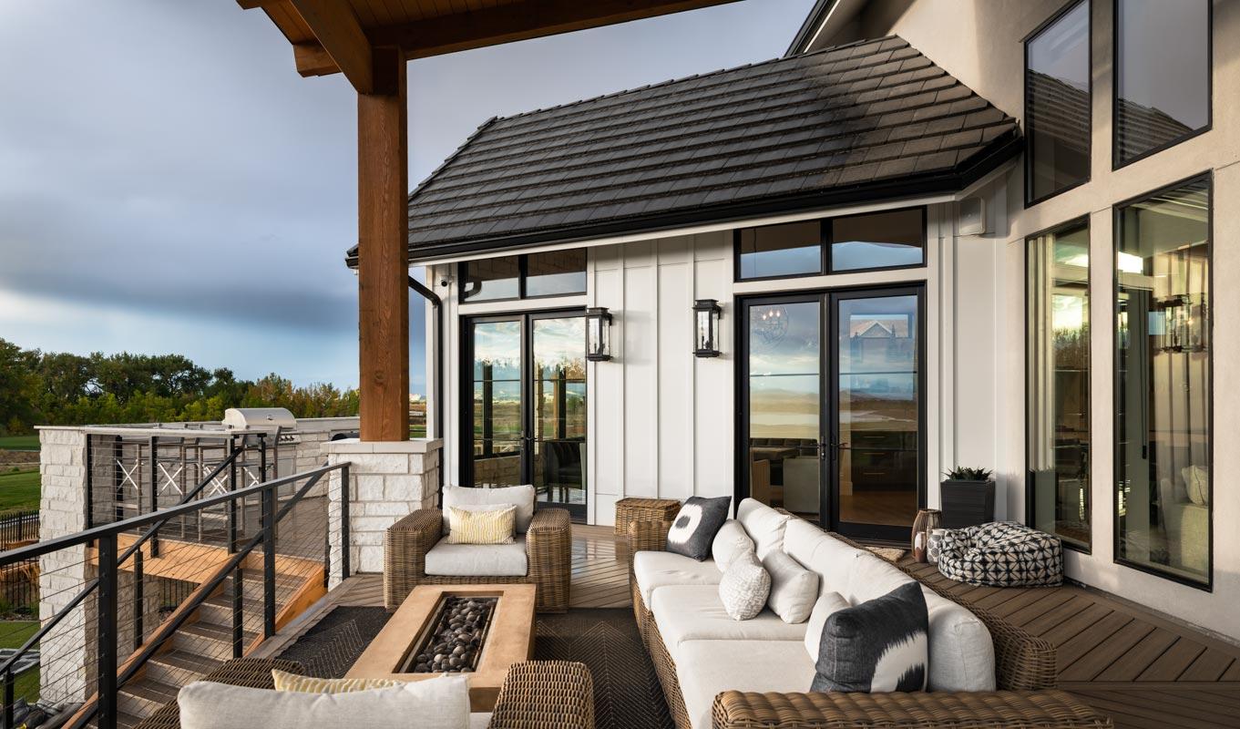 House plan exterior featuring white board and batten siding, dark-framed windows, covered patio with outdoor seating, and built-in grill.
