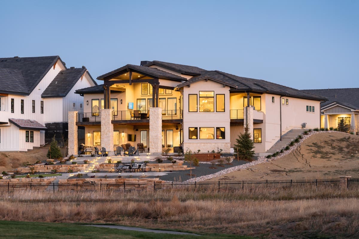 House plan exterior of a modern luxury home with multiple levels, covered balconies, stone columns, and extensive landscaping.