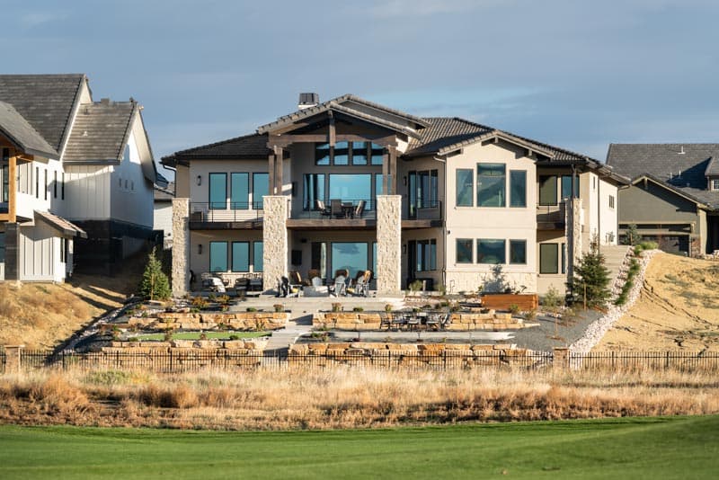 House plan exterior featuring a multi-story modern design with large windows, balconies, stone accents, and a terraced backyard.