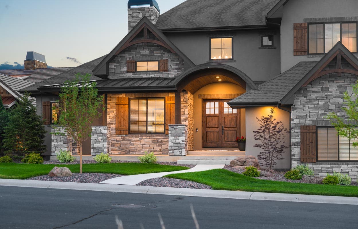 House plan exterior featuring stone and stucco facade, arched entry with double wooden doors, multiple gables, and wood shutters.