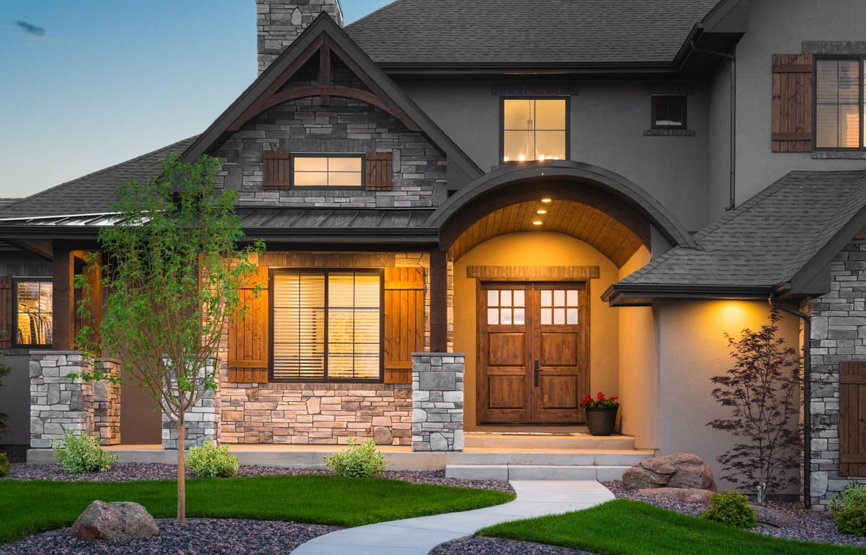 House plan exterior: Two-story home with stone and stucco facade, arched entry with double wood doors, gables, and wood shutters.
