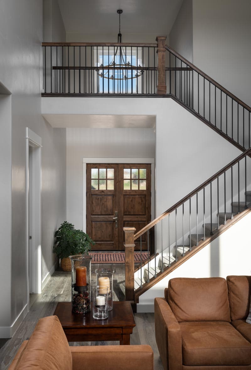 Foyer with double wood doors, staircase with wood newel posts and metal balusters, and second-story balcony railing.