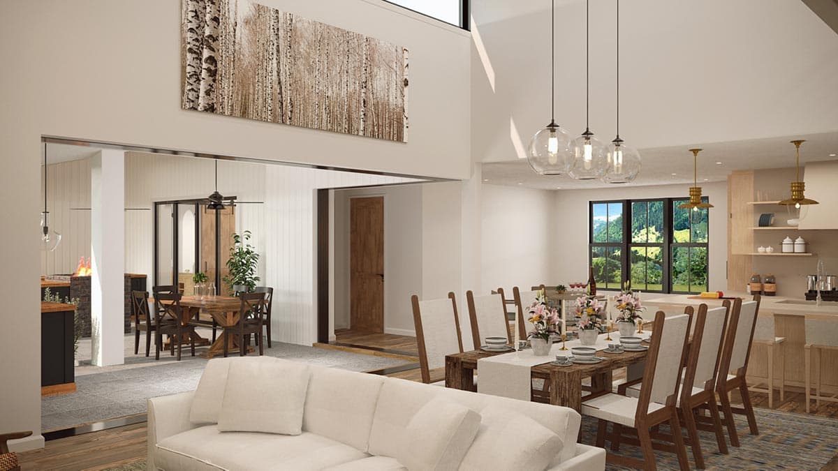 Open concept living area with dining table, kitchen island, and seating, featuring vaulted ceilings and large windows.
