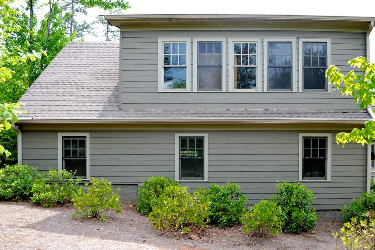 House plan exterior with gray horizontal siding, a gambrel roof, and multiple double-hung windows with grids.