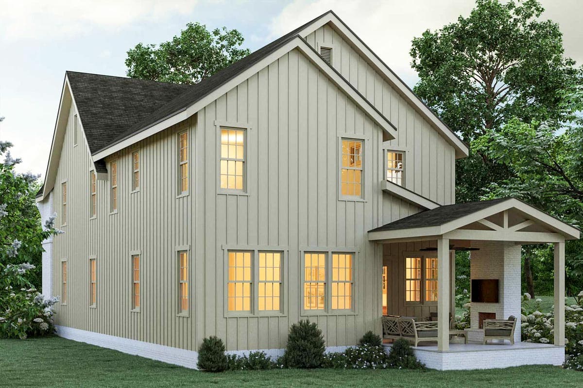A two-story house with light-colored siding, a dark roof, and a covered porch. Warm light glows from windows, suggesting interior lighting.