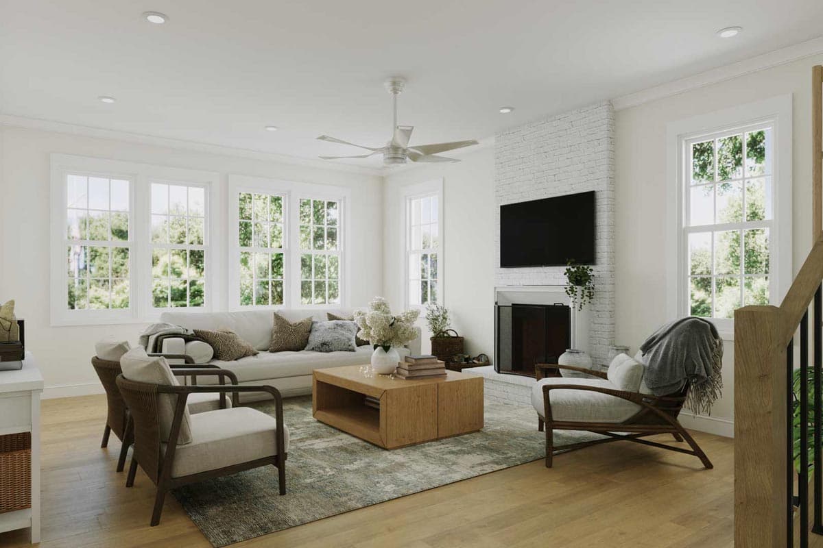 A bright living room features a white sofa, two armchairs, a wooden coffee table, and a fireplace with a mounted television.
