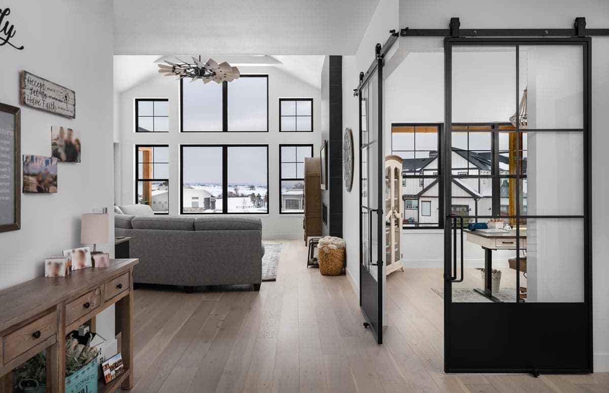 Spacious, modern living room with large windows overlooking a snowy landscape. A black framed glass sliding door leads to an adjacent room.