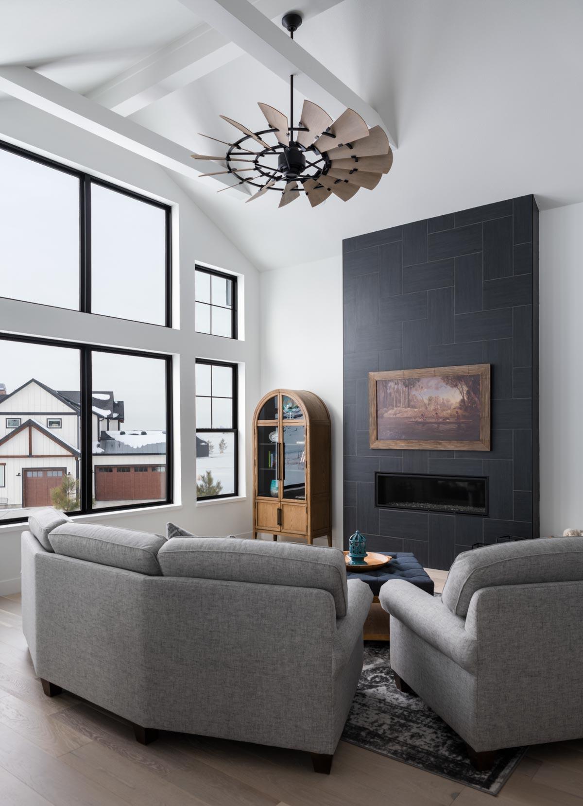 A modern living room featuring a statement black tile fireplace and large windows showcasing an outdoor winter scene.