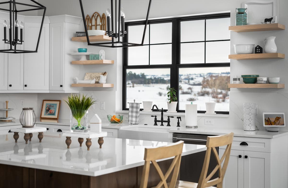 Bright, modern kitchen with white cabinetry, a large island, and a sink beneath a window overlooking a snowy landscape.