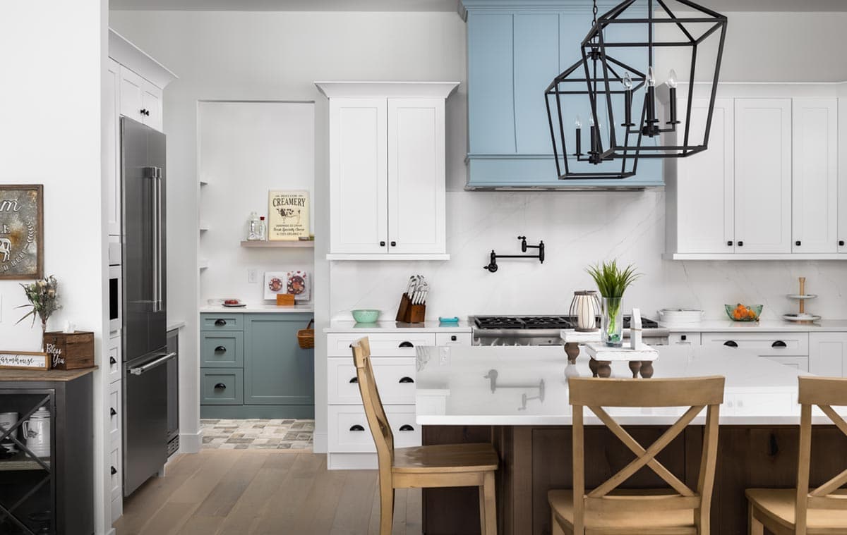 A modern kitchen features white cabinets, a large island with wooden chairs, and a stylish black light fixture hanging above.