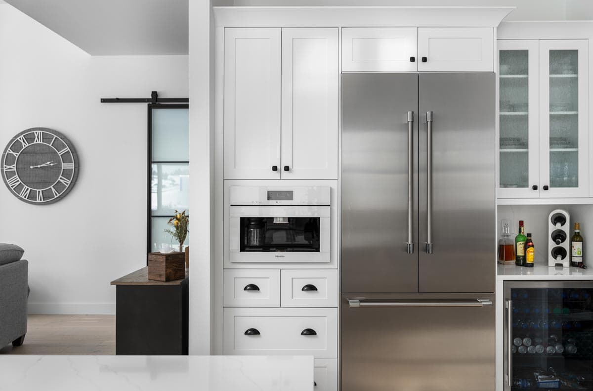 Modern kitchen featuring white cabinetry, a stainless steel refrigerator, and a built-in coffee machine. A large clock is on a nearby wall.