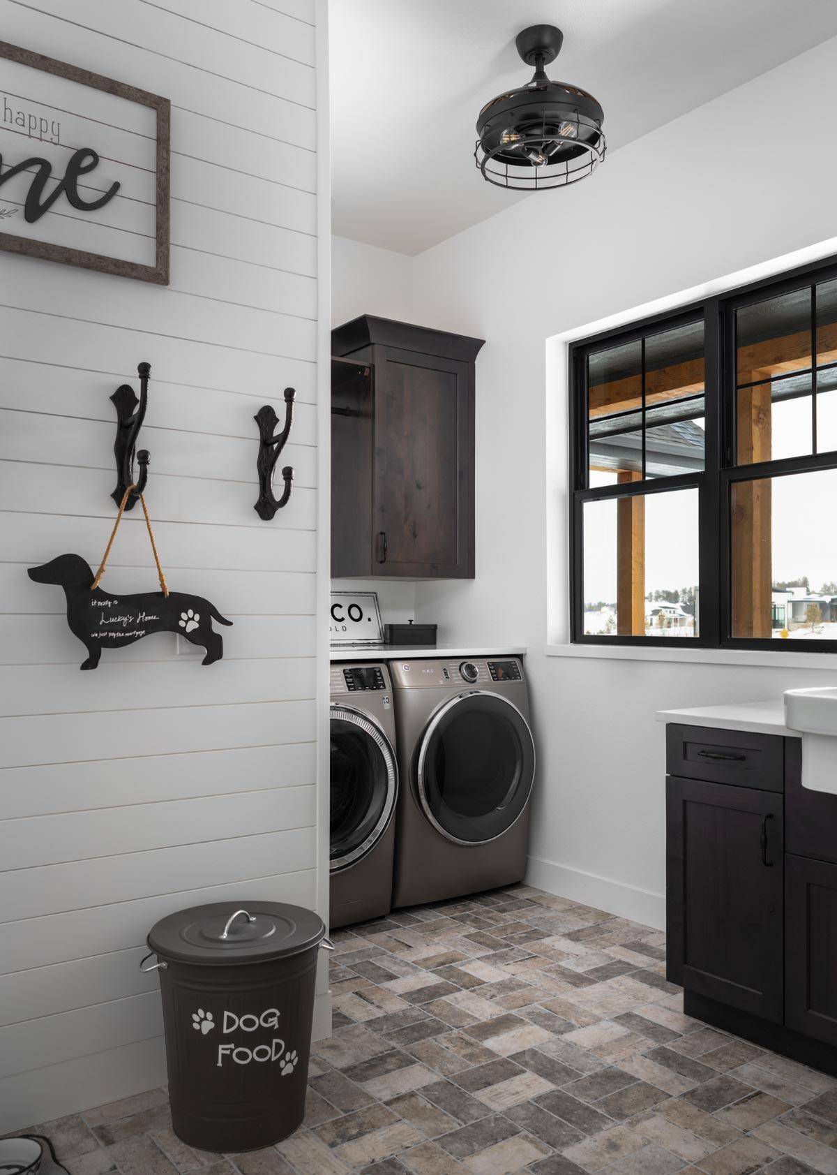 A laundry room features a dog-themed sign and decor, with a sign that says, “Lucky's Home.” Washers and a dryer are visible, along with a window.
