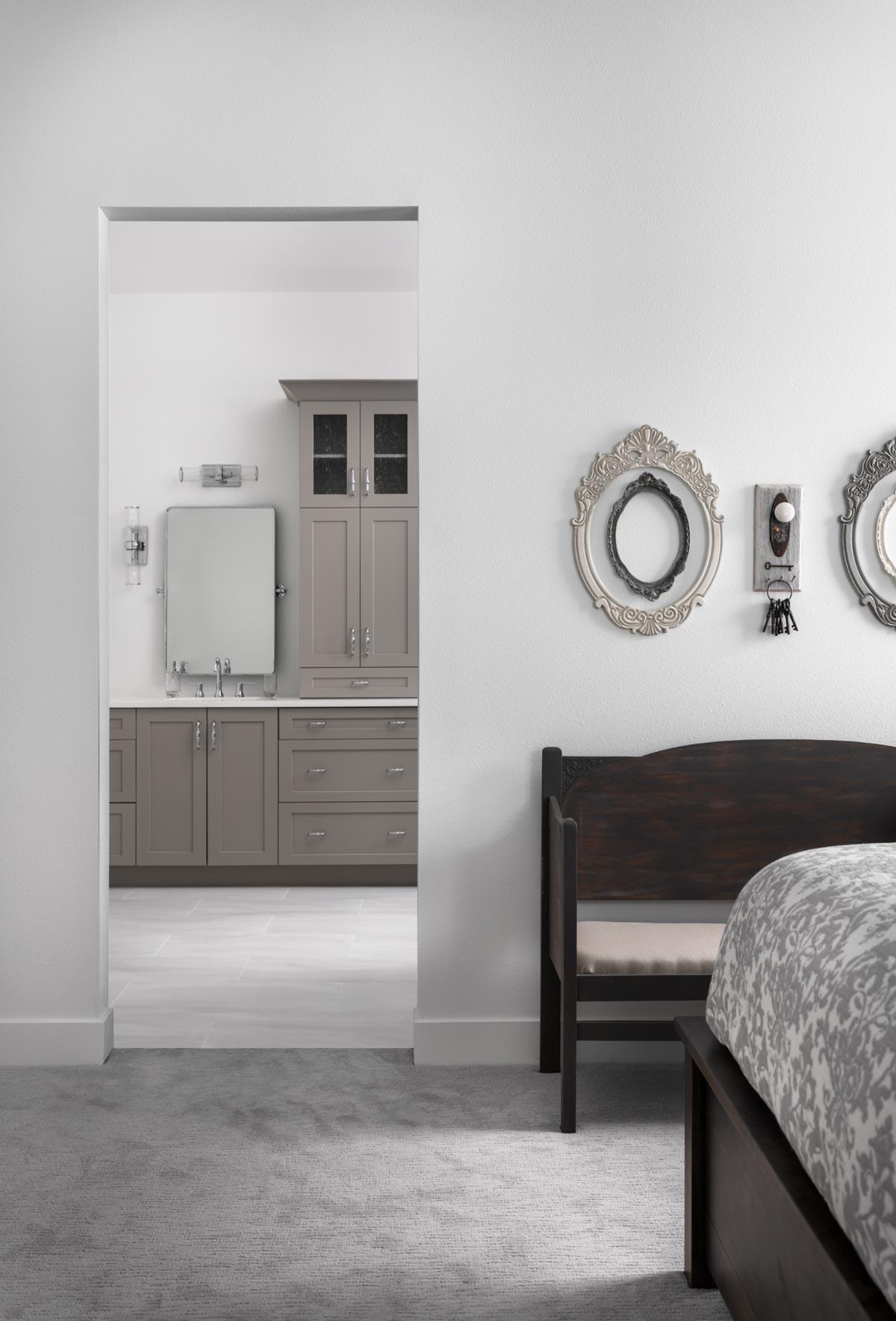 A bedroom interior reveals a bathroom entrance. Ornate frames hang on the wall, a dark wooden bench sits near the bed with patterned bedding.
