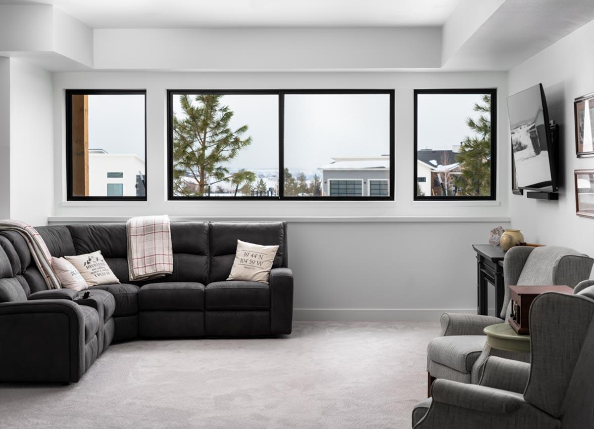 A modern living room with a gray sectional sofa, two armchairs, and large windows overlooking a snowy landscape.