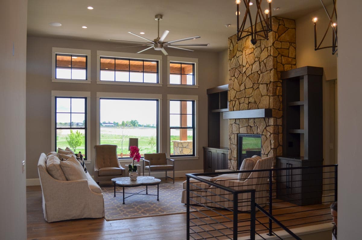 Great room with stone fireplace, built-in shelving, large windows, and a ceiling fan.