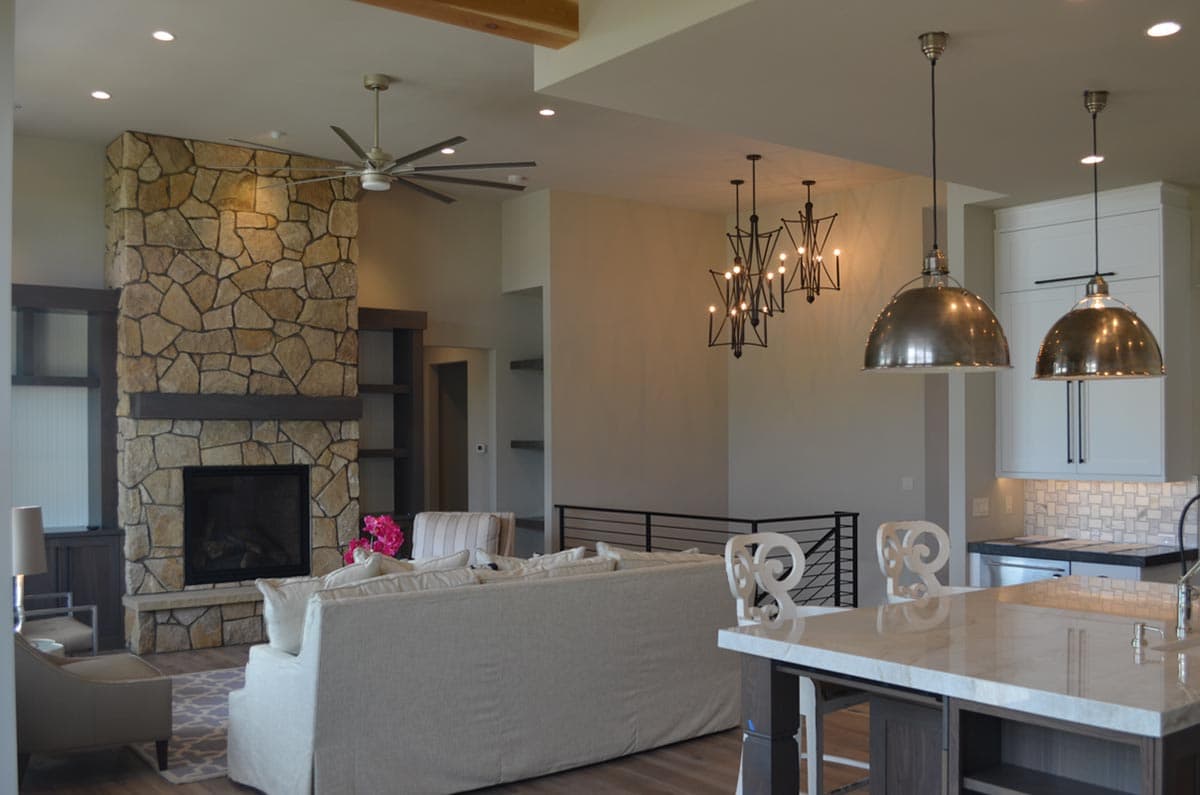 Interior view of an open-concept living and kitchen area with a large stone fireplace, vaulted ceiling, and pendant lighting.