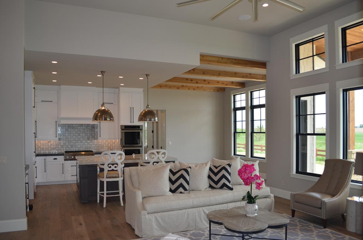 Interior view of an open-plan living area and kitchen with exposed wood beams, large windows, and a kitchen island.
