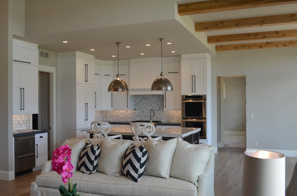 Modern kitchen with white cabinets, island, decorative tile backsplash, and exposed wooden ceiling beams.