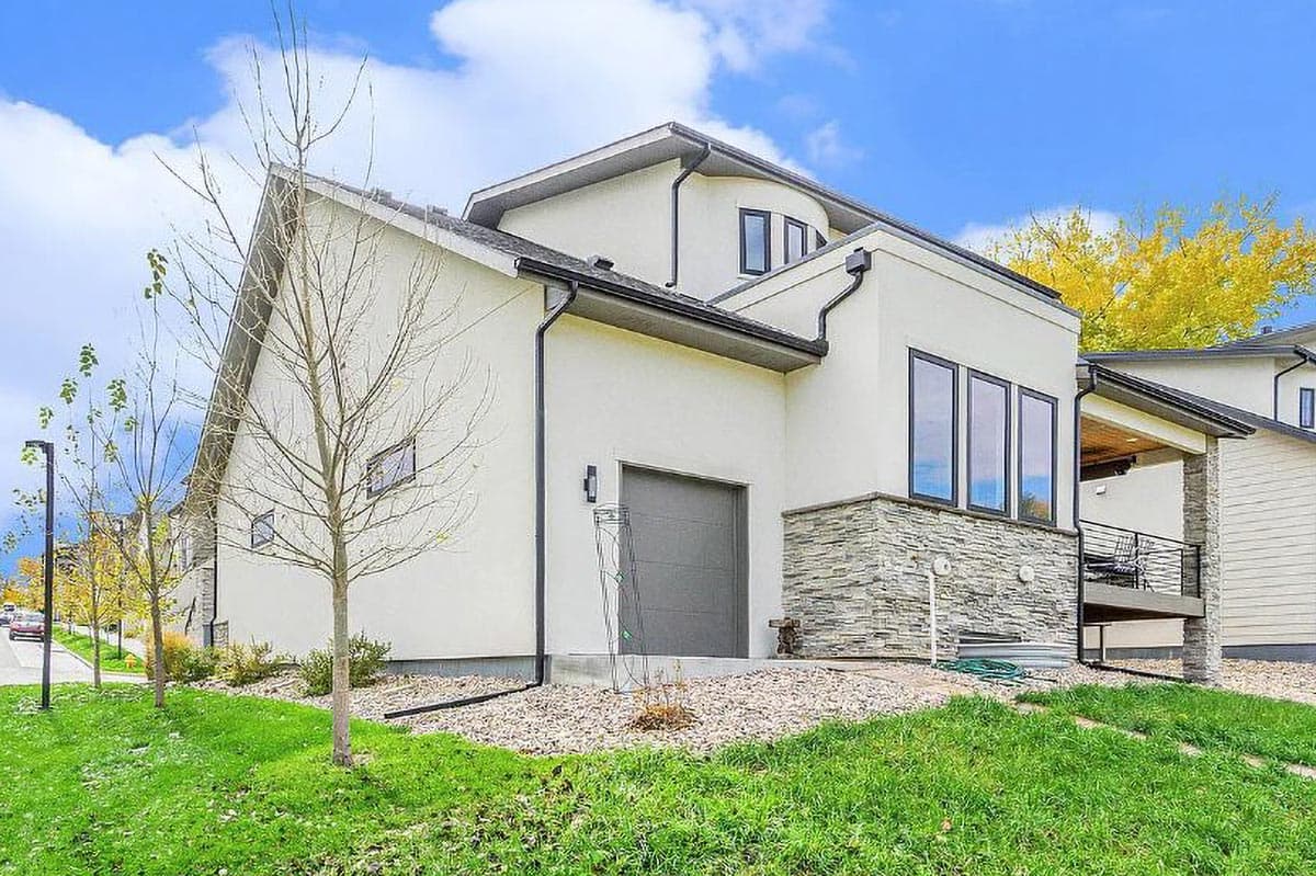 Modern house plan exterior with stucco finish, stone accents, a single garage door, and an upper-level balcony.