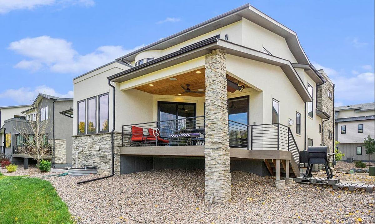Modern house exterior with stucco, stone accents, covered deck with wood ceiling, and metal railings.