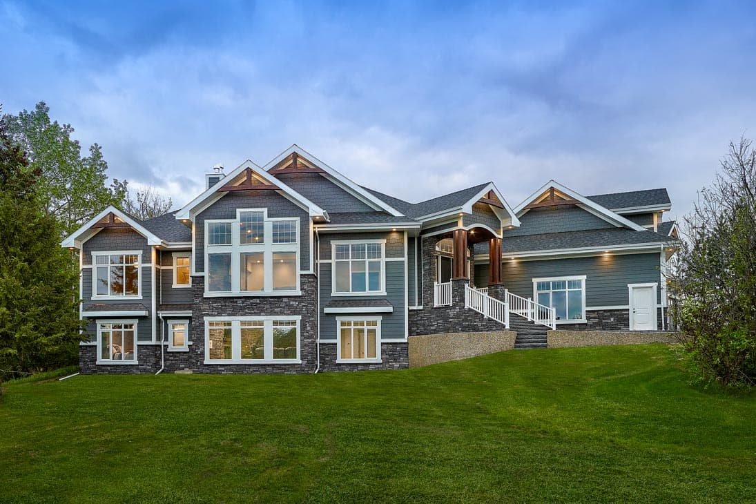 House plan exterior. Two-story Craftsman home with gabled rooflines, stone facade, and a covered entry porch with stairs.