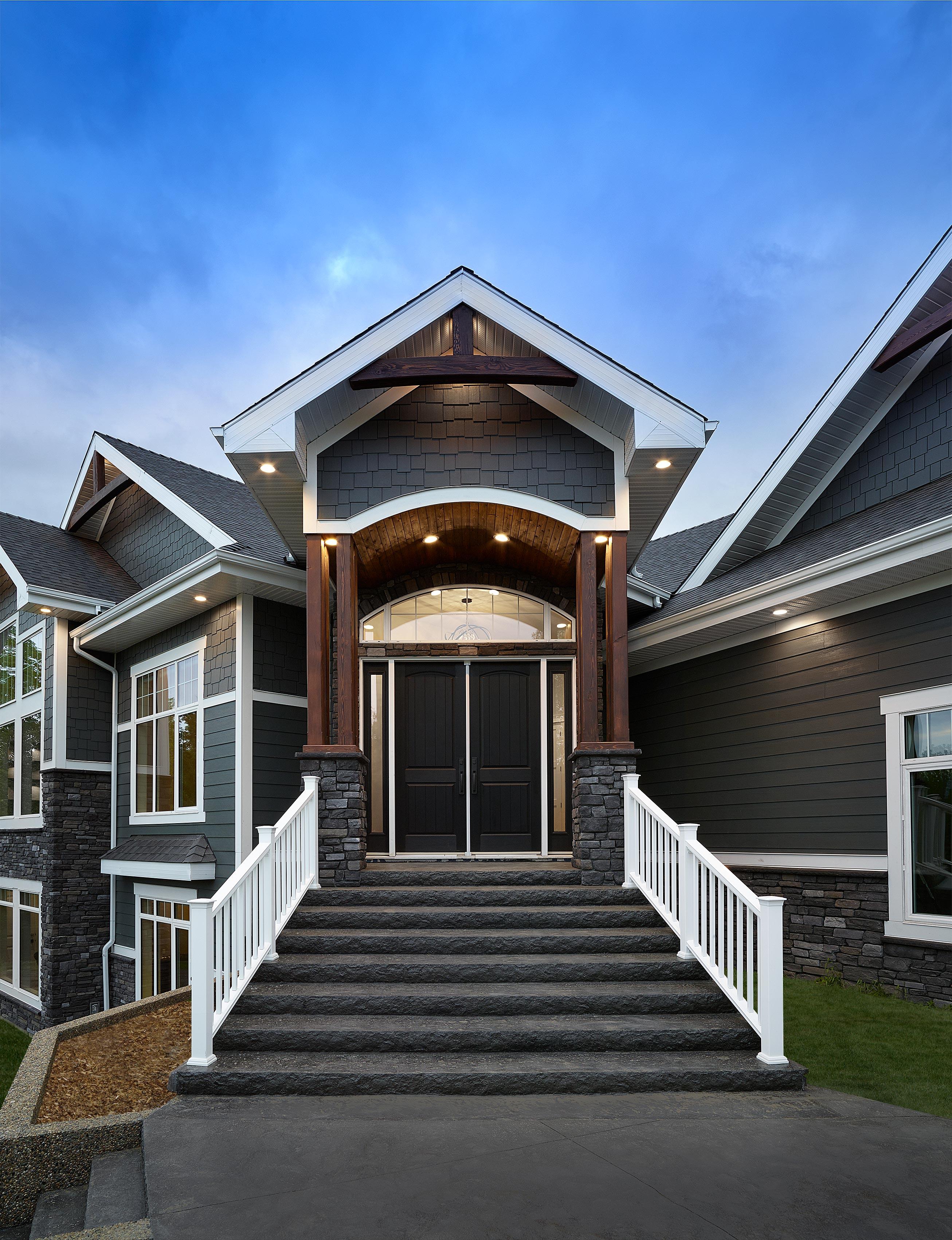 House plan exterior with dark shingle siding, stone accents, gabled rooflines, and a grand arched entryway with double doors.