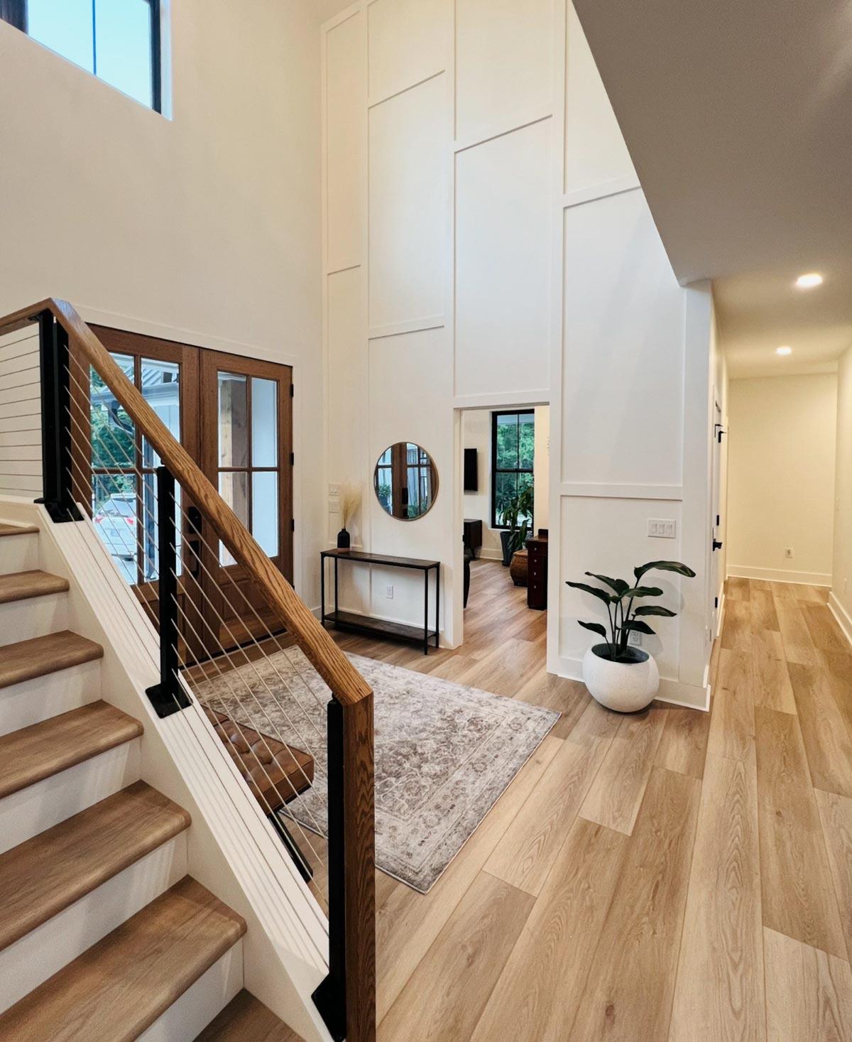 Interior view of a modern entryway with a floating staircase, paneled accent wall, and wood floors.