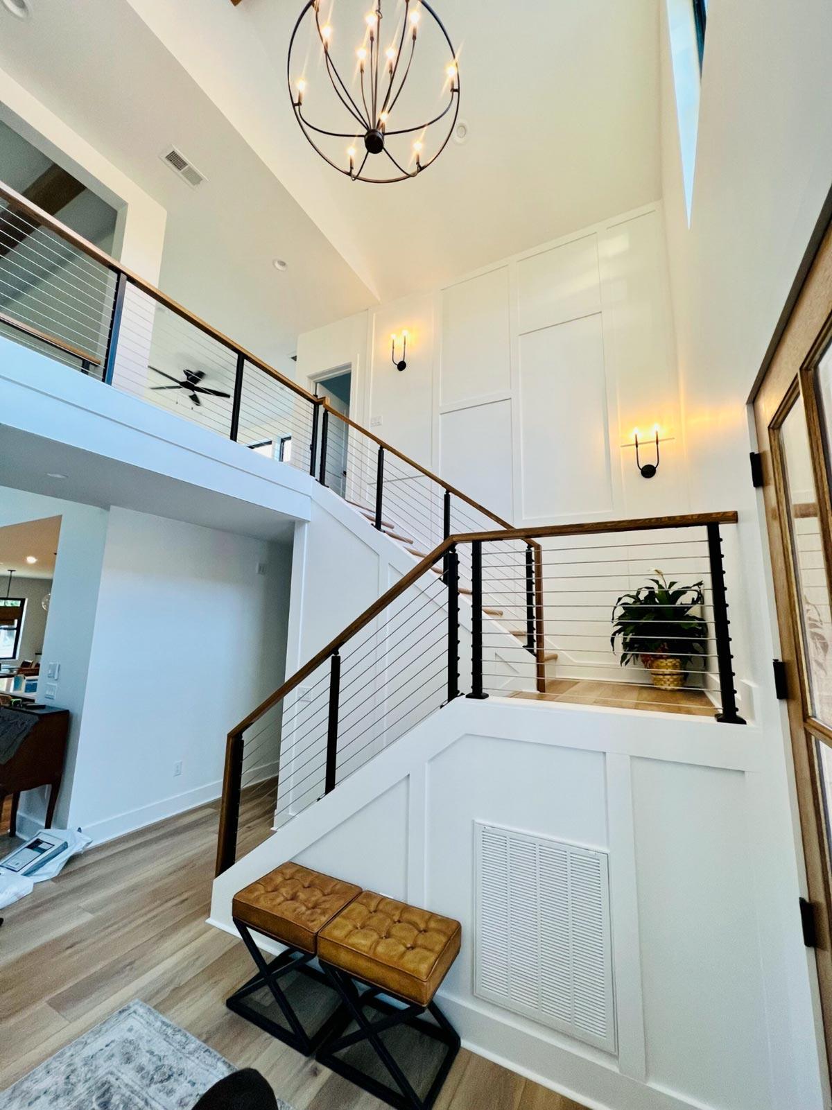Interior view of a two-story foyer with a floating staircase, cable railing, wood handrails, and a modern chandelier.