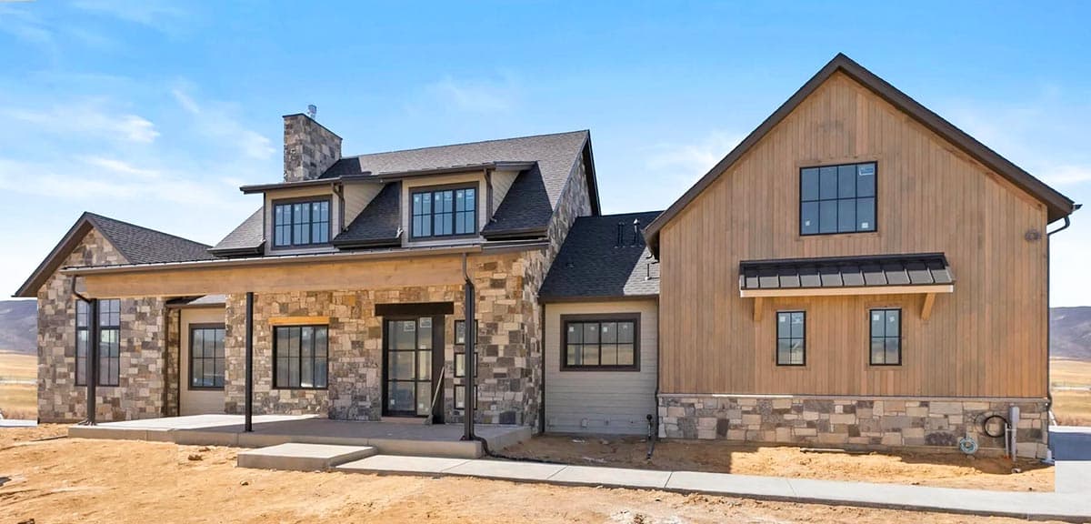 House plan exterior. Modern farmhouse style with stone and wood siding, covered porch, dormers, and gables.