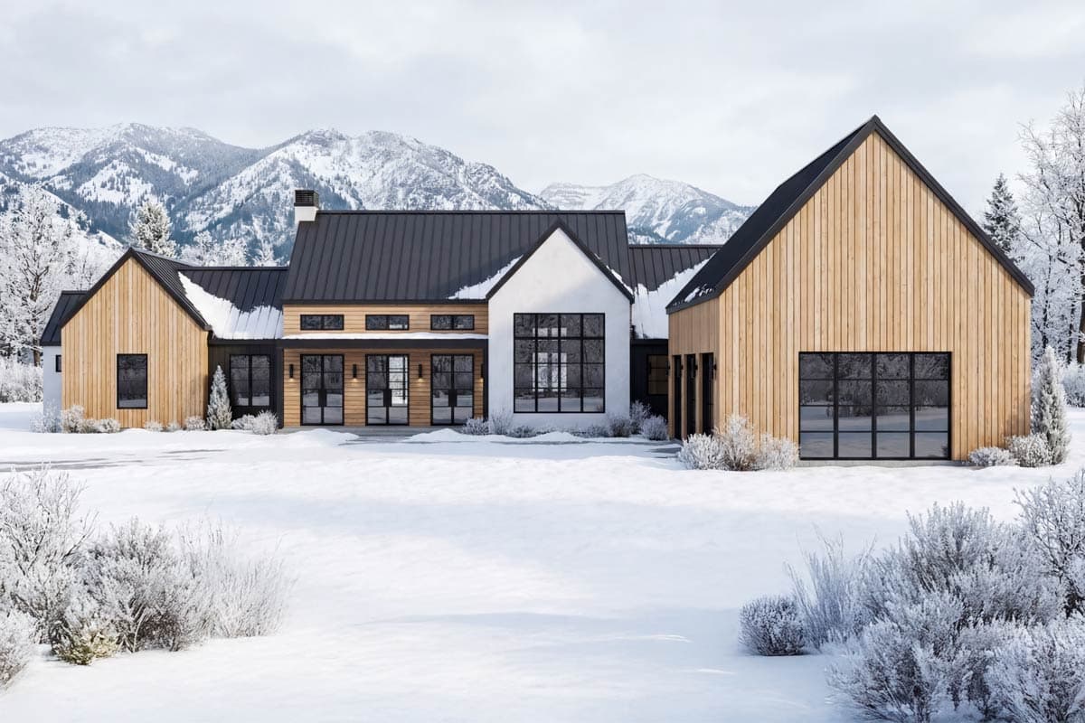 A modern, multi-winged home with wood siding and a black metal roof sits in a snowy landscape, framed by snow-covered mountains.