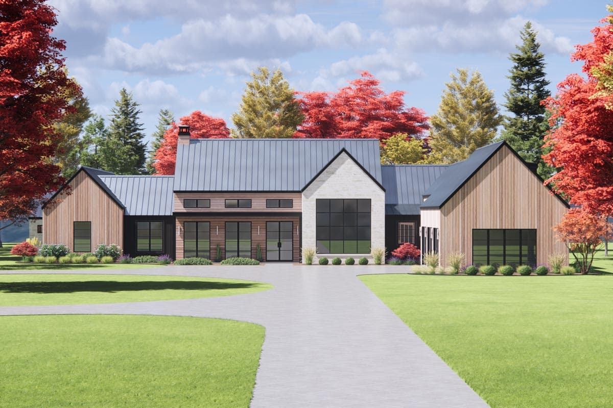 A modern home with a long driveway surrounded by green lawn and colorful trees. The house features a metal roof, wooden siding, and large windows.