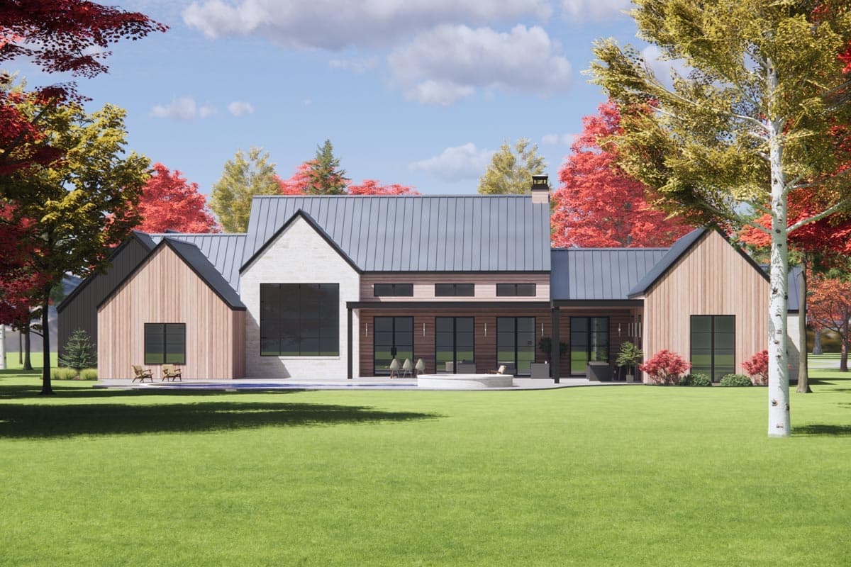 A modern home with a metal roof and light wood siding sits on a large grassy lawn, surrounded by colorful fall trees.