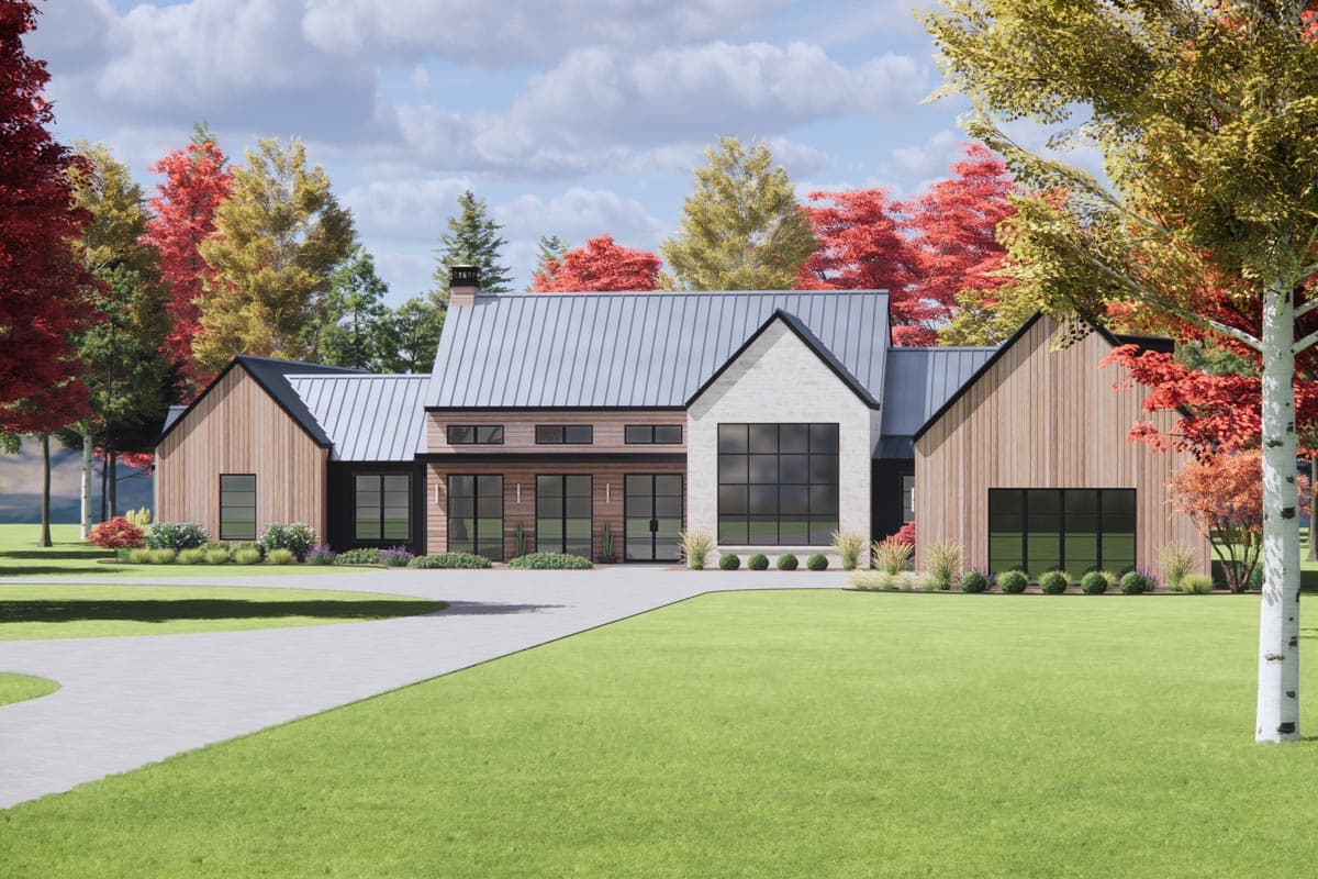 Modern house with stone and wood exterior, large windows, and a metal roof. A curving driveway leads to the house, surrounded by autumn trees.