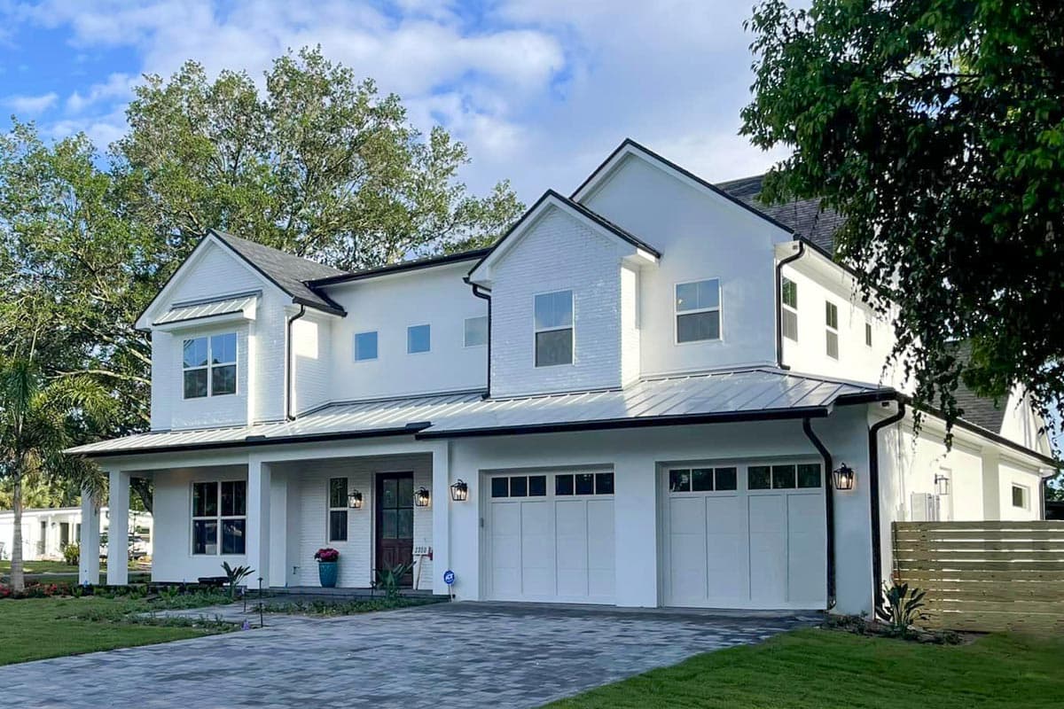 House plan exterior. Two-story Modern farmhouse with a covered porch, gabled roof, and two-car garage. White stucco exterior with black trim.