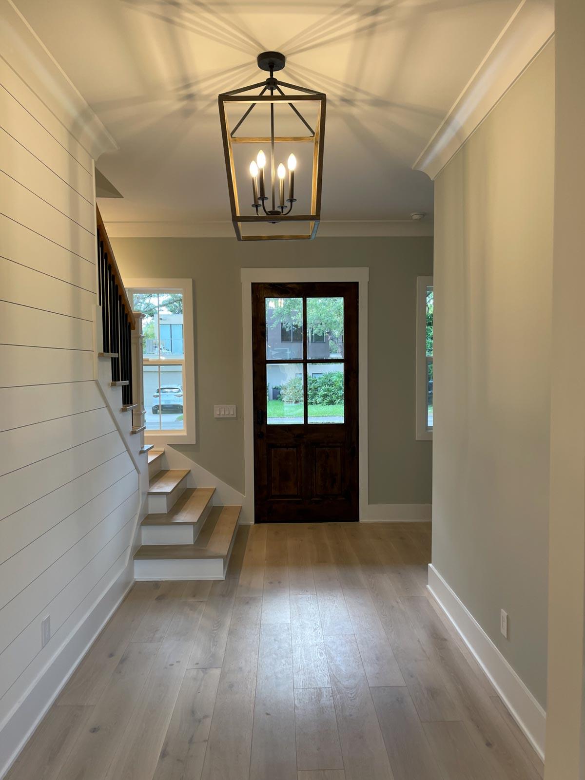 Interior view of entryway with shiplap wall, wood stairs, dark wood door with glass panes, and lantern pendant light.