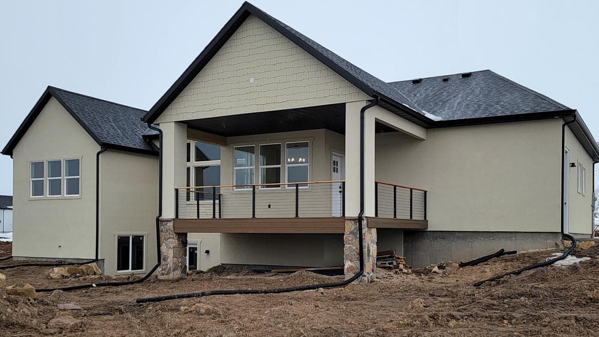 House plan exterior view of a two-story home with a covered deck, stone-accented columns, and shingle siding.