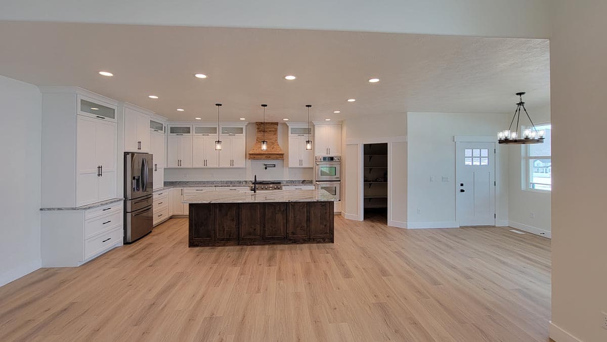 Spacious kitchen with white cabinets, large island, and wood range hood. Open to dining area with front door.