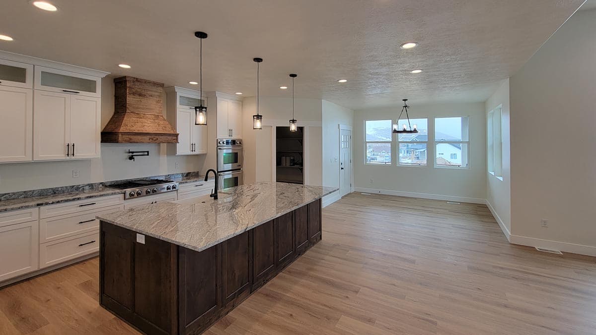 Kitchen with island, range, dual ovens, and wood range hood, open to dining area with large windows.